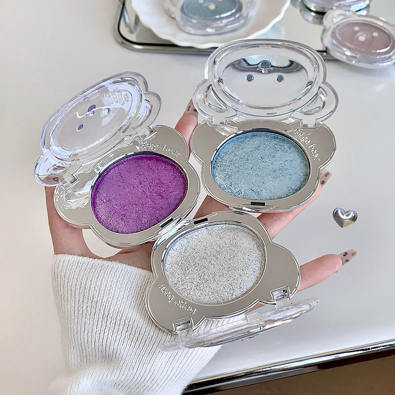 Three compact makeup cases with purple, blue, and silver contents held by a hand.
