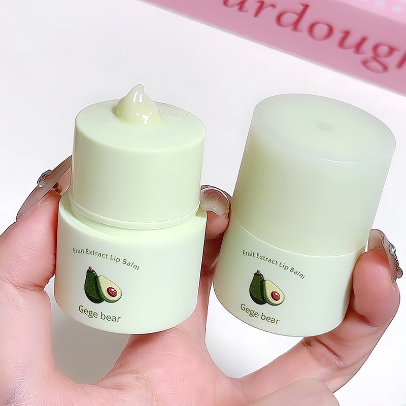 Two small green lip balm containers held in a hand with a blurred background.