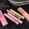 Set of GEGE BEAR lip glosses on a dark surface with a basket in the background.