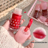 Red nail polish bottle with matching lip color, held by a hand, with a small basket of nail polishes in the background.