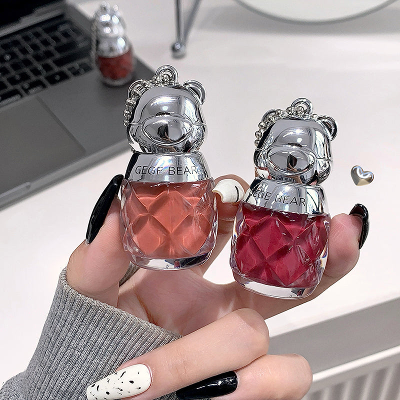 Two small bear-shaped bottles with red liquid held by a person's hand.