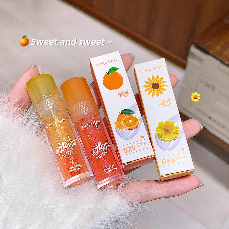Two lip glosses and their packaging held by a hand on a soft surface.