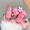 Pink blush stick with floral design held by a hand against a neutral background