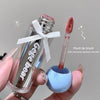 Clear lip balm with pink cap and fluffy applicator held by a hand against a neutral background