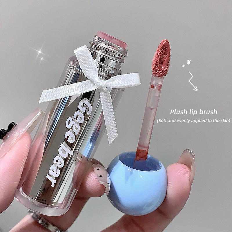 Clear lip balm with pink cap and fluffy applicator held by a hand against a neutral background