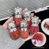 Red jelly-like bear-shaped containers with silver lids held by a hand, set against a blurred background.