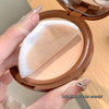 Compact powder with a sponge applicator held by a hand on a wooden surface.