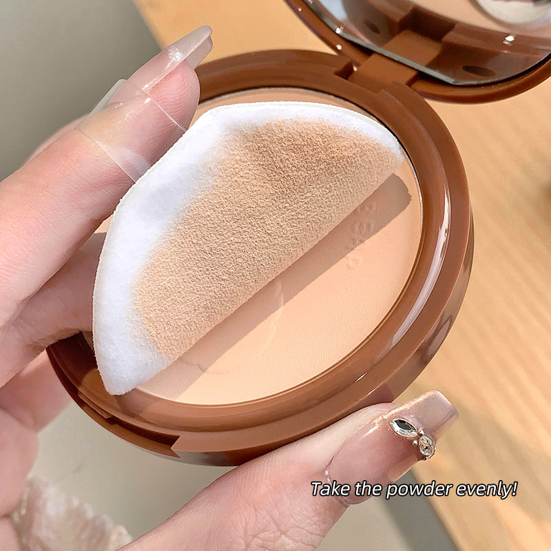 Compact powder with a sponge applicator held by a hand on a wooden surface.