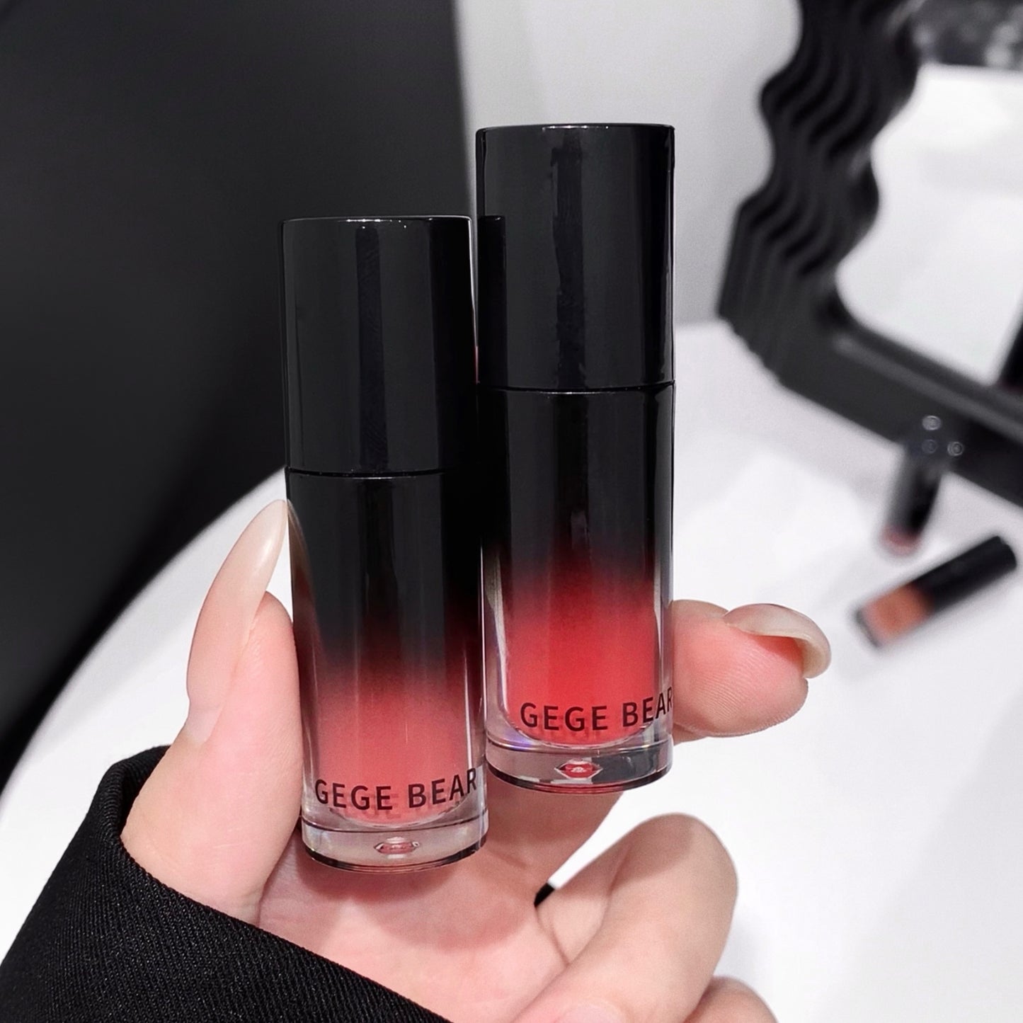 Two lip products with gradient design held by a hand, brand 'GEGE BEAR' visible.