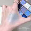 Hand with glittery makeup swatch in front of a blue eyeshadow palette