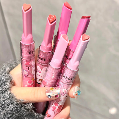 Five pink lip balms with cartoon designs held by a hand against a neutral background