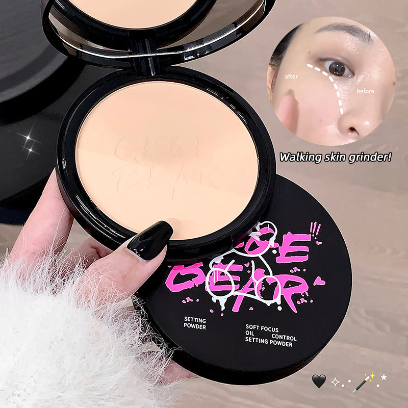 Compact powder with brand logo and text, held by a hand with black nail polish.