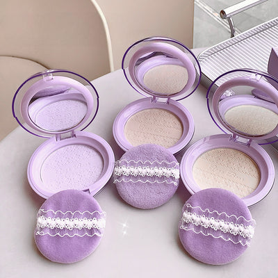 Purple makeup compacts with lace designs on a white surface