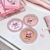 Three round compact powder cases with cartoon designs on a white surface.