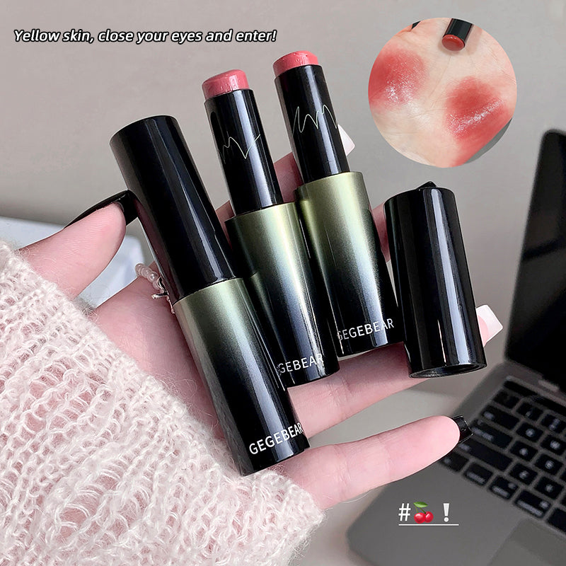 Three lipsticks held in a hand with a laptop in the background