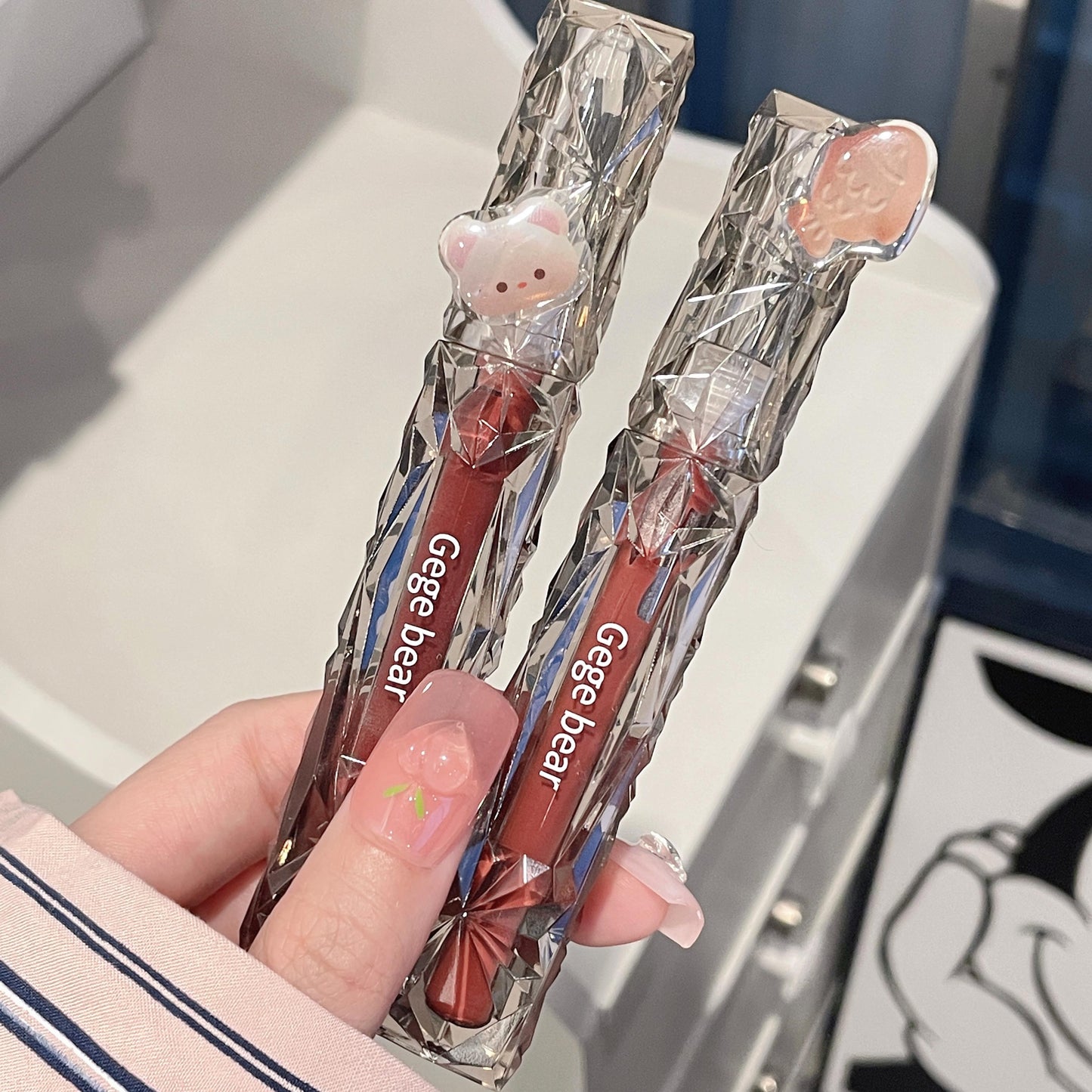 Two Gege bear lip balms in clear wrappers held by a hand.