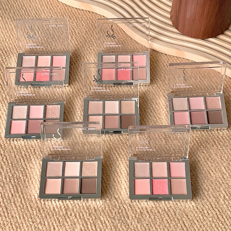 Multiple makeup palettes with shades of pink, brown, and beige on a textured surface.
