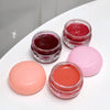 Four small jars of lip balm in different colors on a white surface.