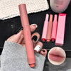 Lipstick held by a hand with other lipsticks and a box in the background