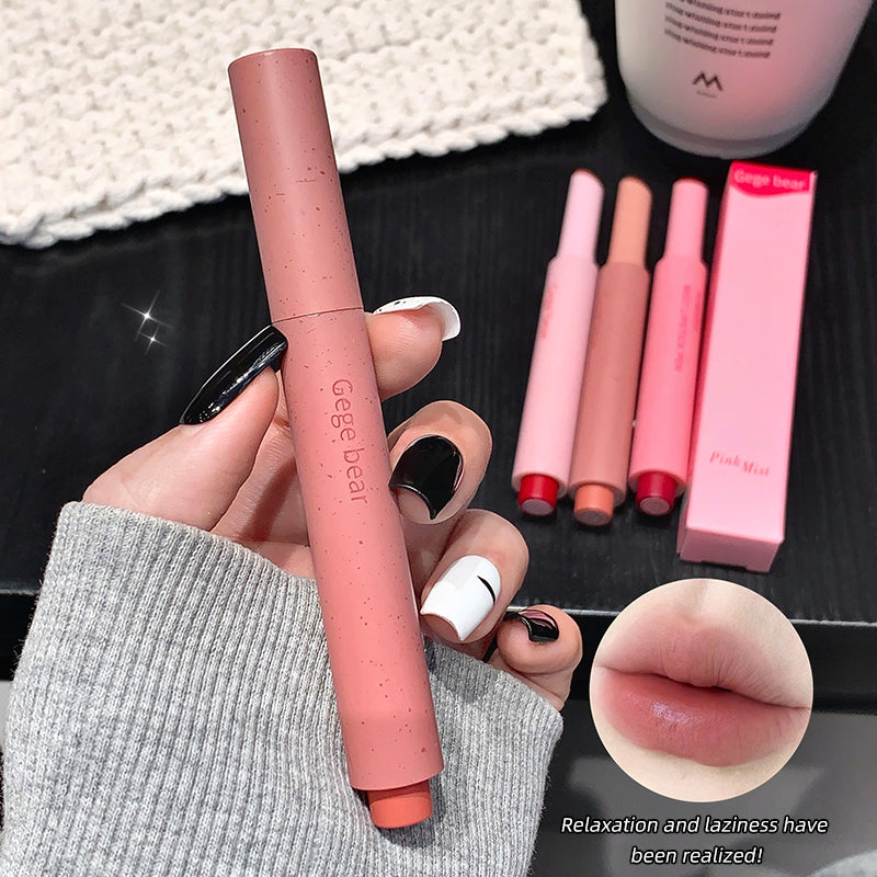 Lipstick held by a hand with other lipsticks and a box in the background