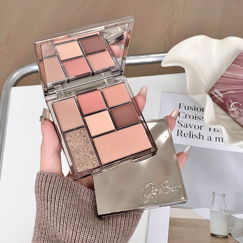 Makeup palette with multiple shades held by a hand, with a magazine in the background.