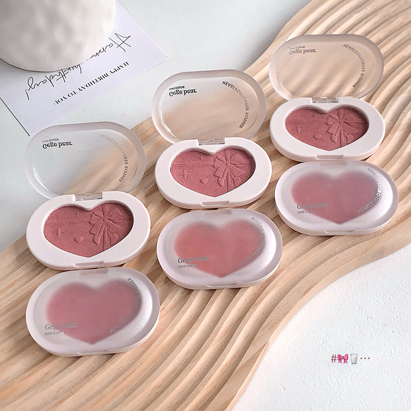 Heart-shaped blush compact with pink blush on a wooden surface