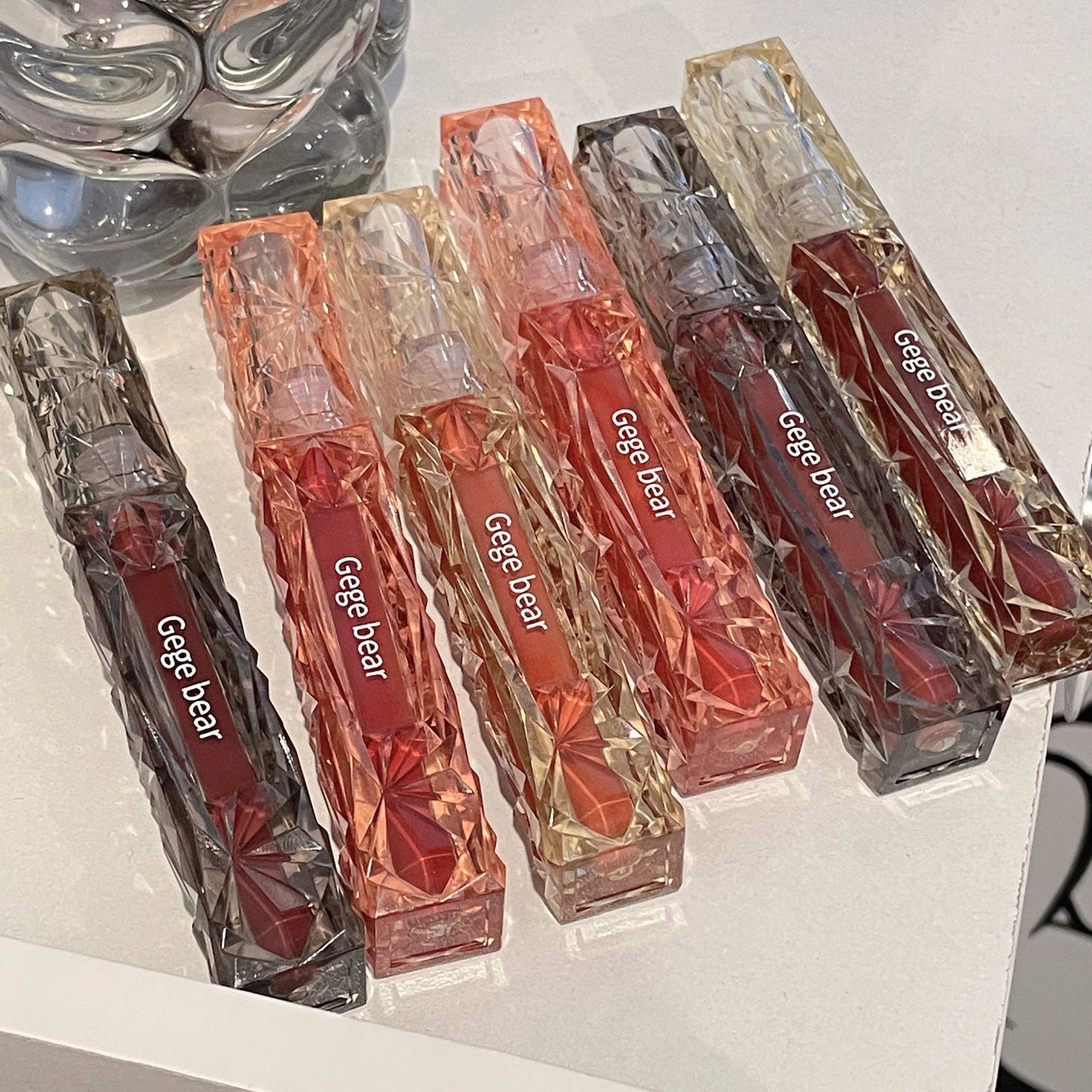 Set of Gege bear lip glosses in clear packaging on a white surface.