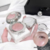 Compact powder with pink glittery shade held by a hand, with a blurred background.