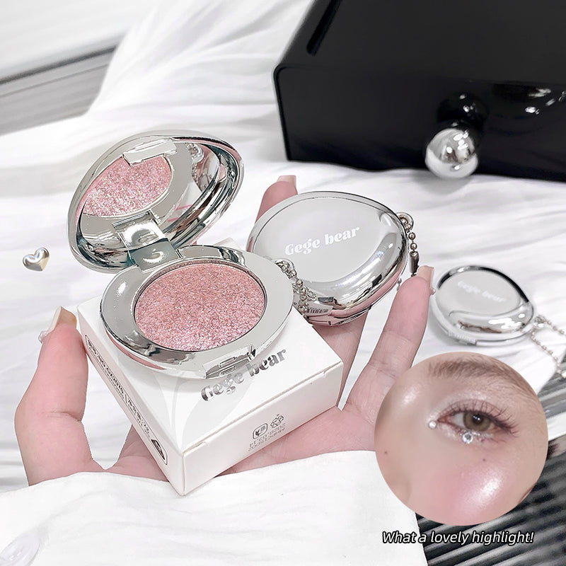 Compact powder with pink glittery shade held by a hand, with a blurred background.