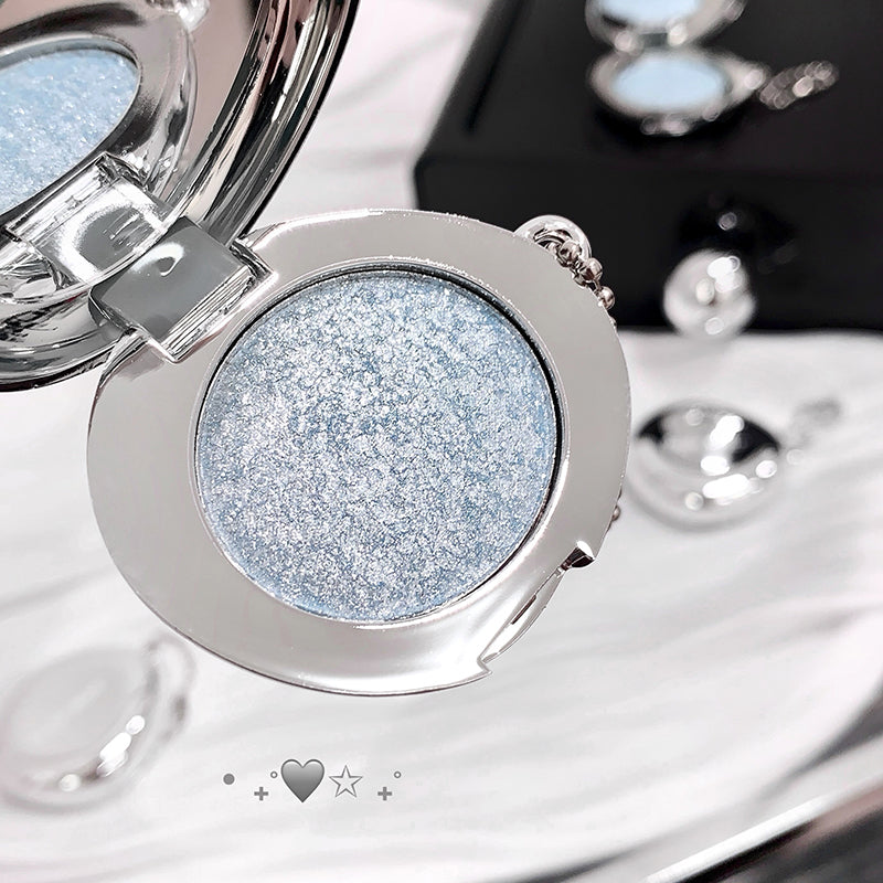Compact powder with blue glittery shade in a silver case on a reflective surface.