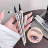 Two GEUGEBAEER eyebrow pencils held by a hand with a close-up of an eye and eyebrow on a desk.