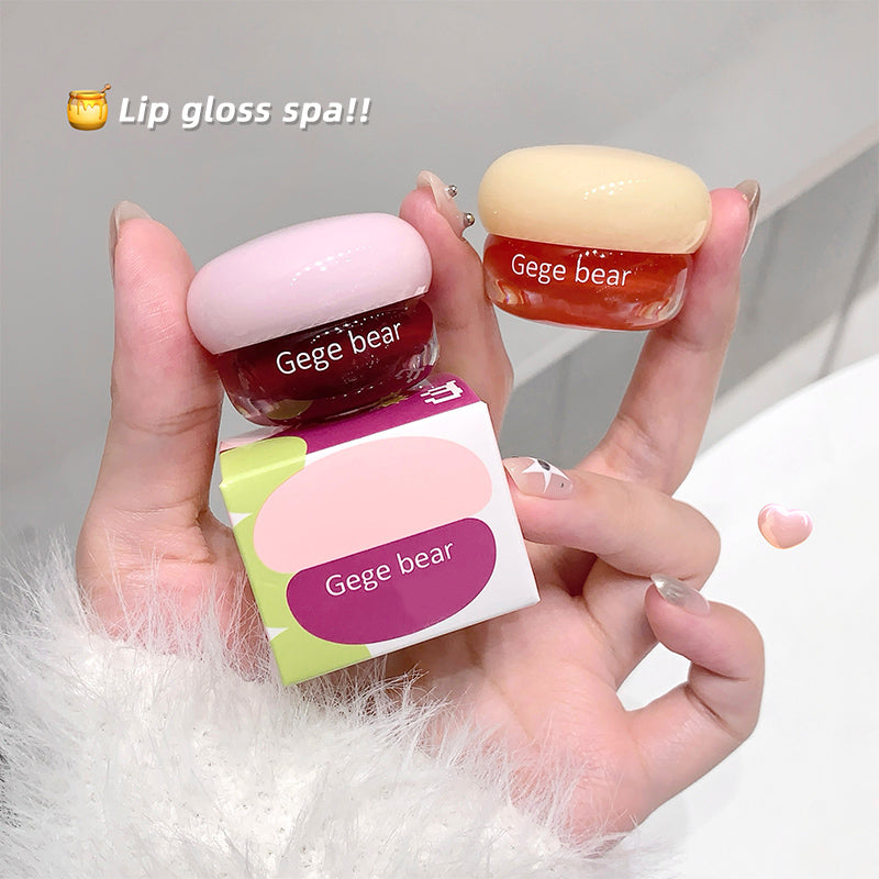 Two lip glosses and their packaging held by a hand with a plain background