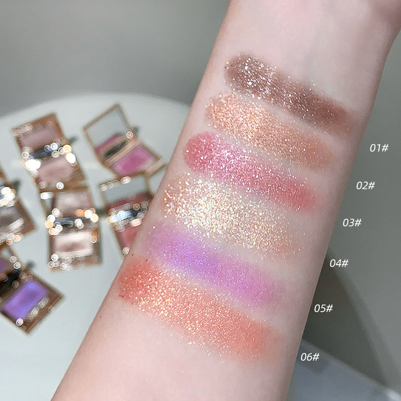 Color swatches of glittery makeup on a person's arm with compact mirrors in the background.