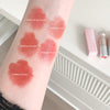 Lipstick swatches on a person's arm with labeled colors, next to lipsticks on a white surface.