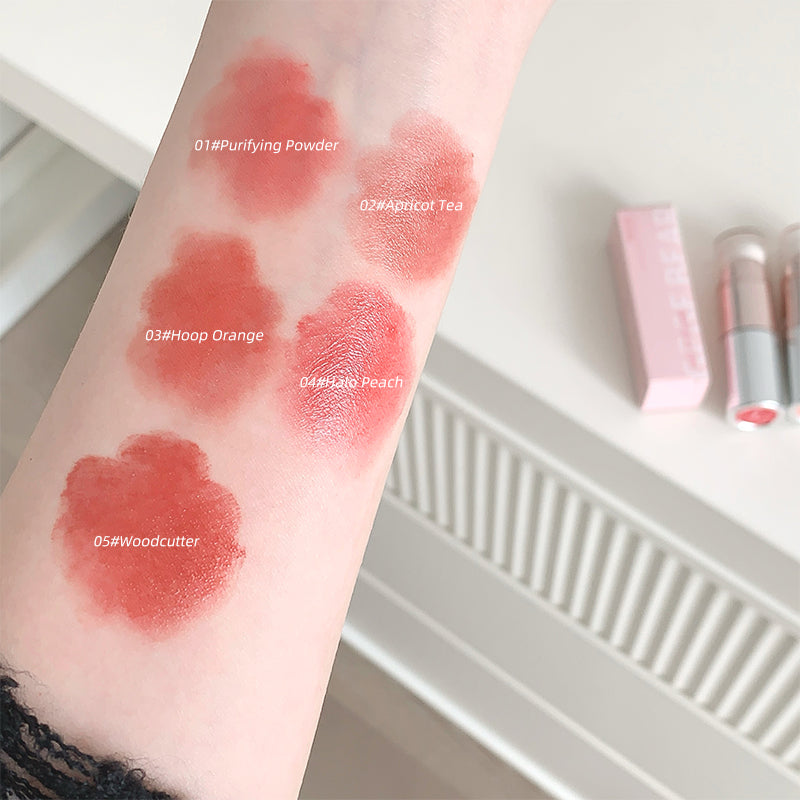 Lipstick swatches on a person's arm with labeled colors, next to lipsticks on a white surface.