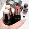 Hand holding makeup sticks with visible brand name 'DARK LIGHT W', blurred background