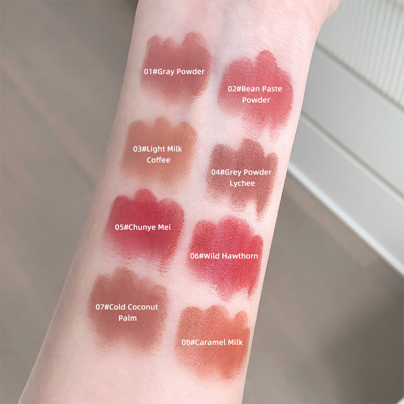 Lipstick swatches on a person's arm with color names and codes.