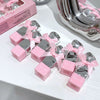 Pink and silver products with ribbons on a white surface, next to a pink box.