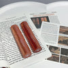 Two red lip glosses on an open book with visible text and images.