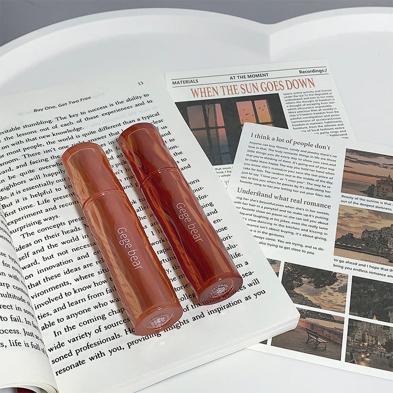 Two red lip glosses on an open book with visible text and images.