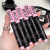Hand holding six black and pink 'Bear' lip glosses with a blurred background