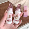 Two small bottles with bear-themed labels held in a hand on a wooden surface.