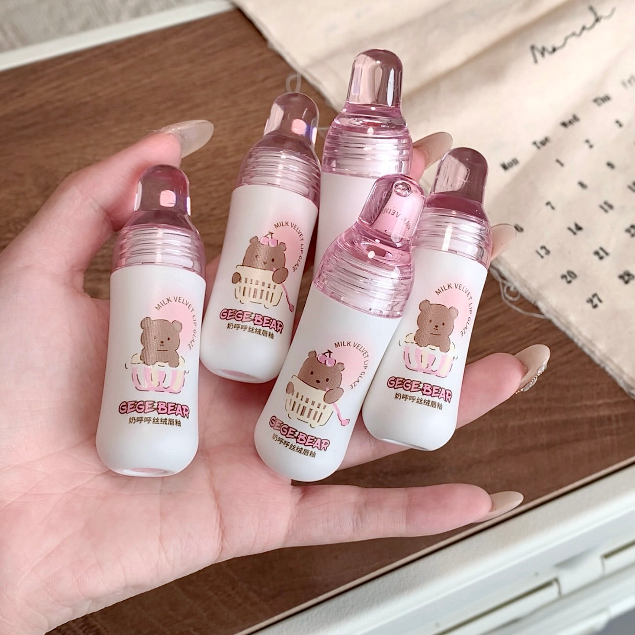 Hand holding five small bottles with bear illustrations on a wooden surface