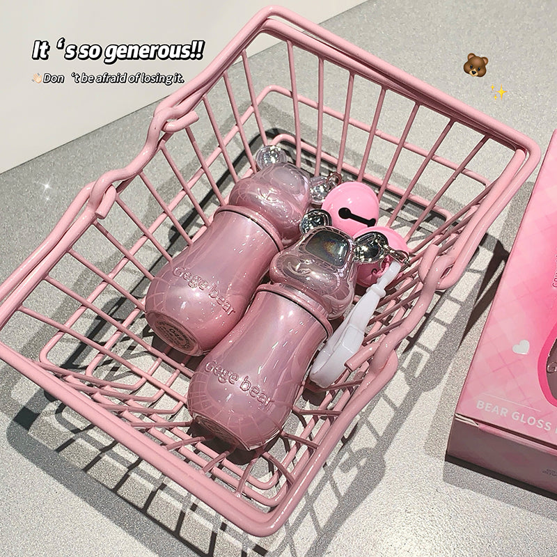 Pink lip gloss set in a pink metal basket on a light gray surface.