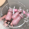 Pink baby bottle-shaped keychains with 'Gege Bear' branding on a clear glass dish.