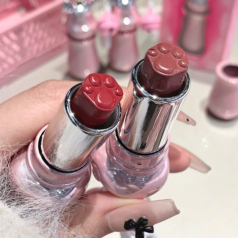 Two lipsticks with paw print caps held by a hand against a pink background.