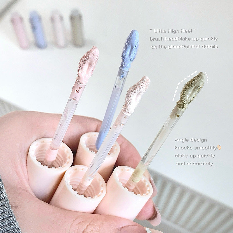 Four cosmetic brushes with different bristle designs held in a hand against a blurred background.