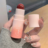 Hand holding a blush stick with 'George Brown' branding, against a blurred indoor background.
