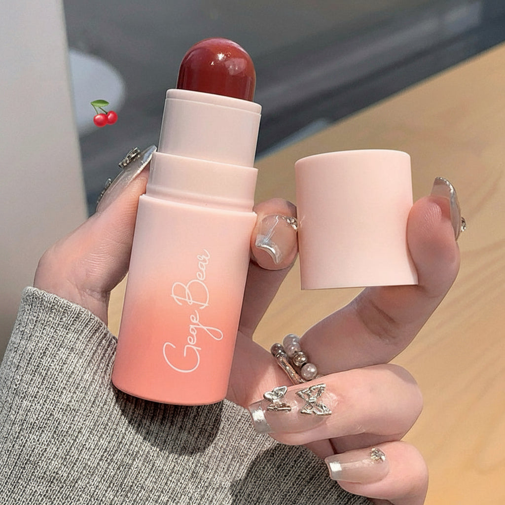 Hand holding a blush stick with 'George Brown' branding, against a blurred indoor background.