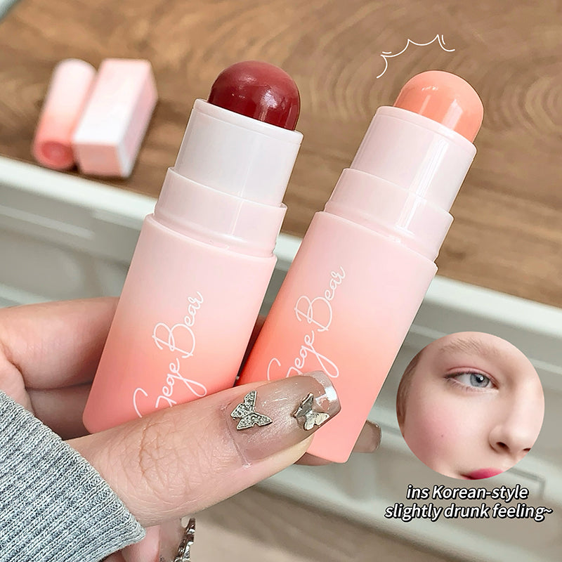 Two pink lip balms with gradient colors held by a hand on a wooden surface.